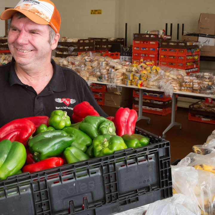 Worker holding a crate of red and green capsicums.